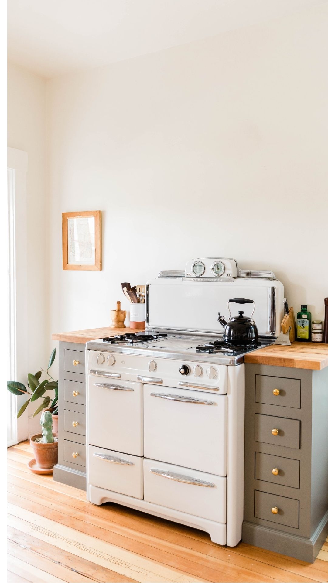 Small-white-light-beige-kitchen-with-a-vintage-style-gas-stove-floor-flower-black-kettle-and-a-wall-art