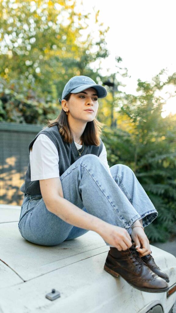 A-woman-sitting-on-top-of-a-car-wearing-casual-wears-for-women-featuring-blue-denim-jeans-navy-blue-top-and-a-white-tee-styled-with-blue-jeans-cap-and-shoe