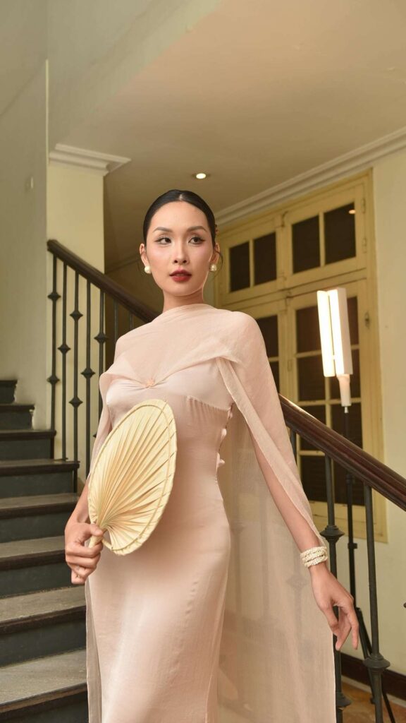 This-dress-code-idea-for-new-year's-party-is-featuring-a-woman-wearing-long-gown-holding-a-hand-made-fan-standing-on-stair-case-prepared-to-go-for-a-new-year-eve-celebration
