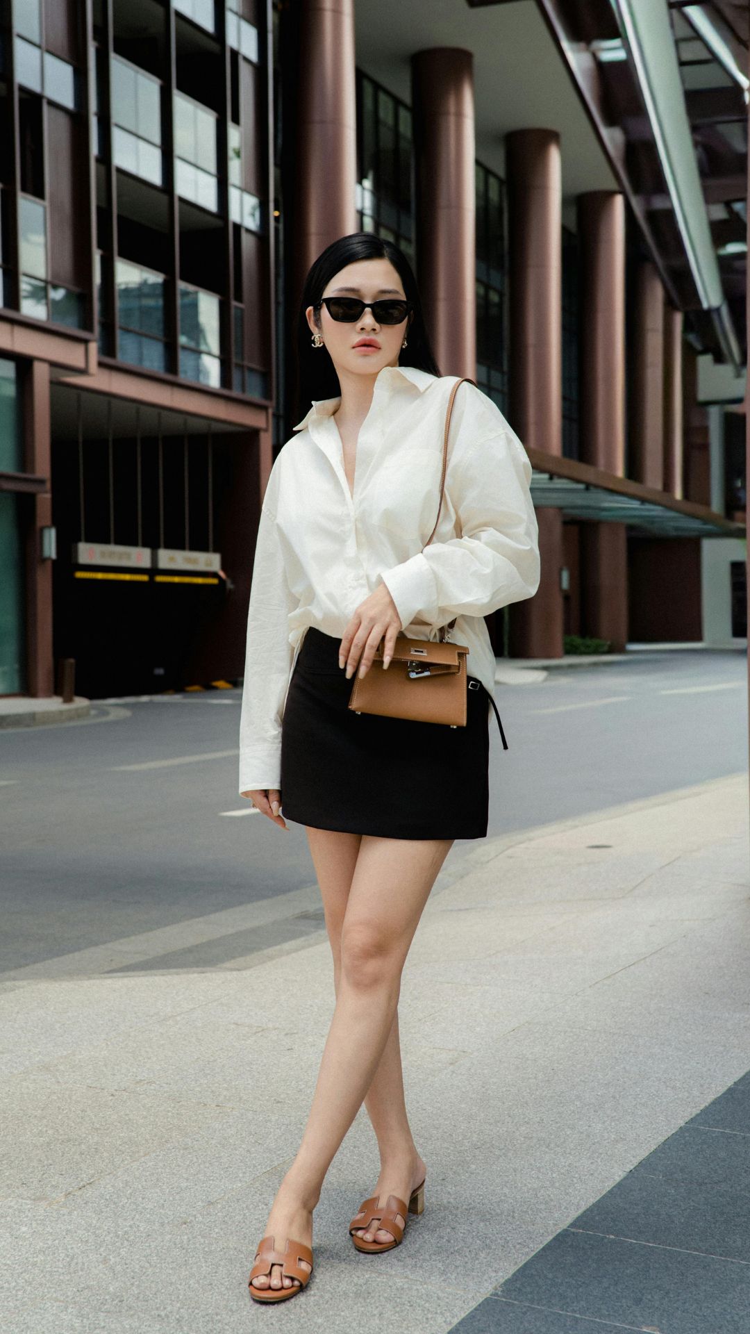 Woman-wearing-a-short-black-skirt-cream-long-sleeve-shirt-carrying-a-brown-handbag-and-wearing-brown-slippers-for-a-date-night-outfit