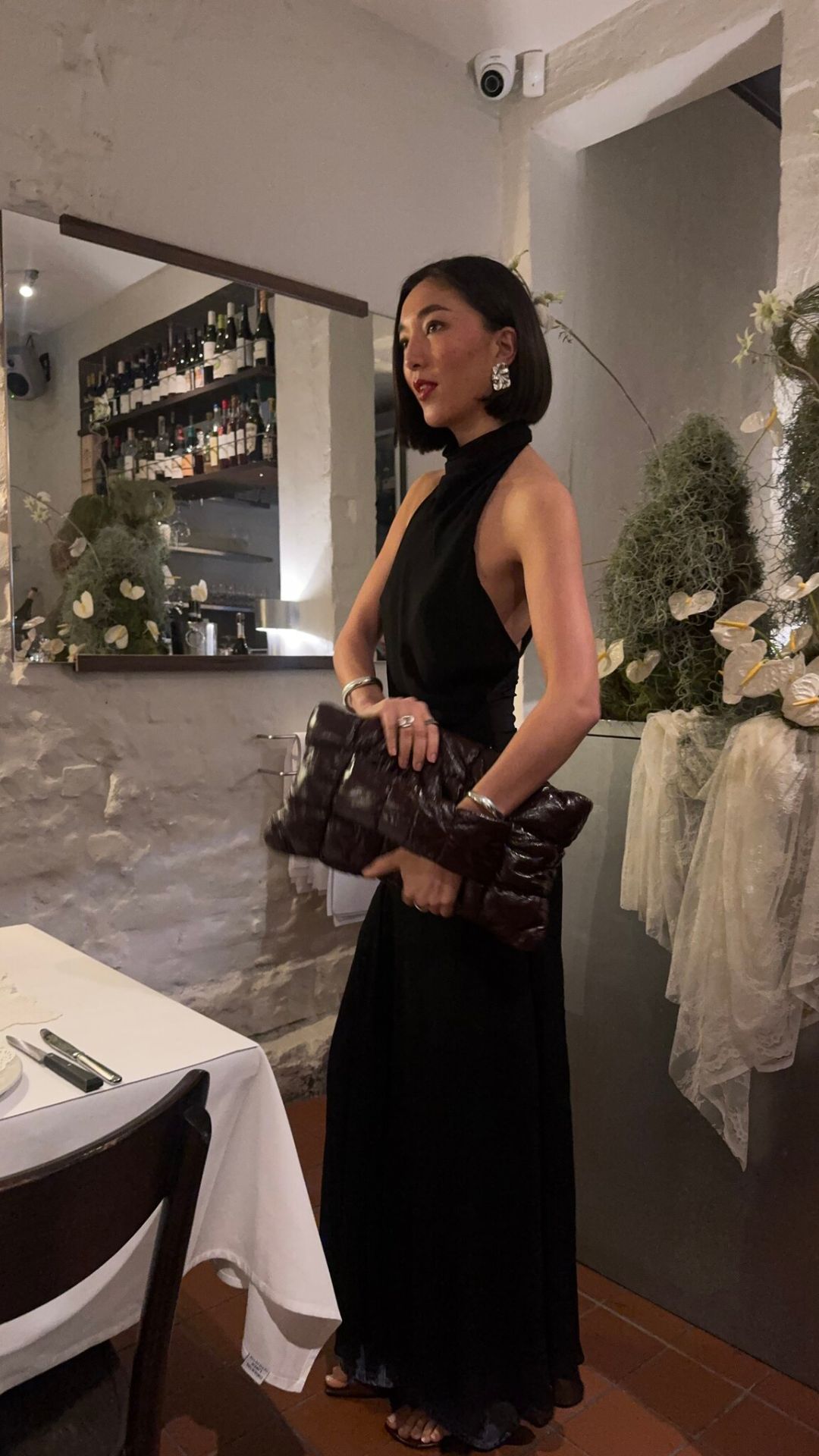 A-woman-wearing-long-black-gown-carrying-a-small-black-handbag-for-a-date-night-and-standing-inside-a-restuarant