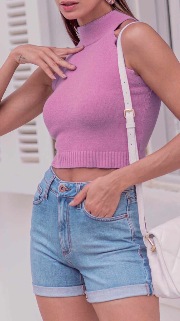 A-woman-wearing-light-fitted-pink-top-and-a-denim-short-with-a-small-white-hand-bag