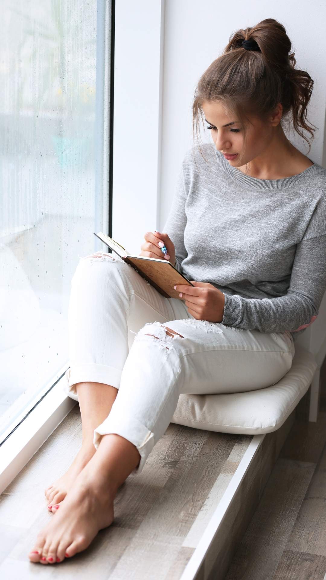 A-featured-image-of-self-care-goals-for-the-new-year-showing-a-woman-sitting-at-the-windoq-journaling-her-new-year-goals