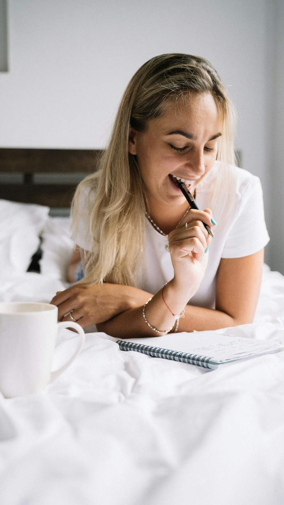 A-woman-lying-down-on-the-bed-while-writing-and-drinking-a-coffee-as-part-self-care-goals-for-the-new-year