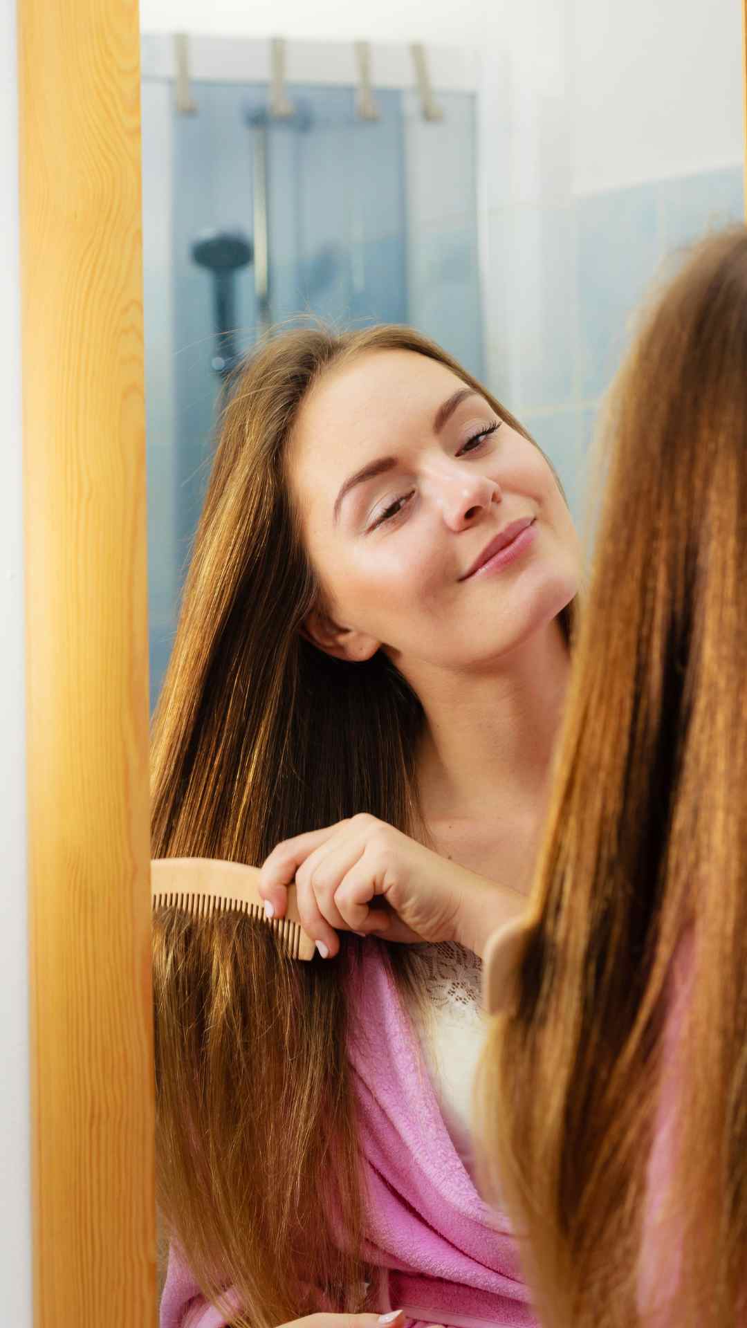 A-woman-standing-in-front-of-a-mirror-brushing-her-hair-happily-after-treating-her-dandruff-scalp-at-home