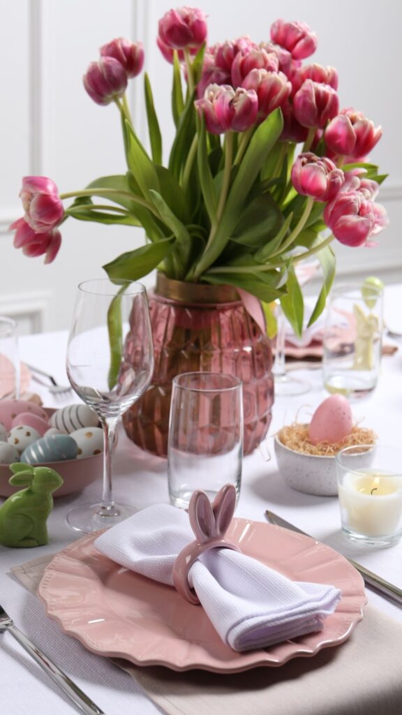 Rose-pink-flower-vase-on-the-table-with-candles-and-scents-including-plates-glass-cup-and-cutleries-on-the-table