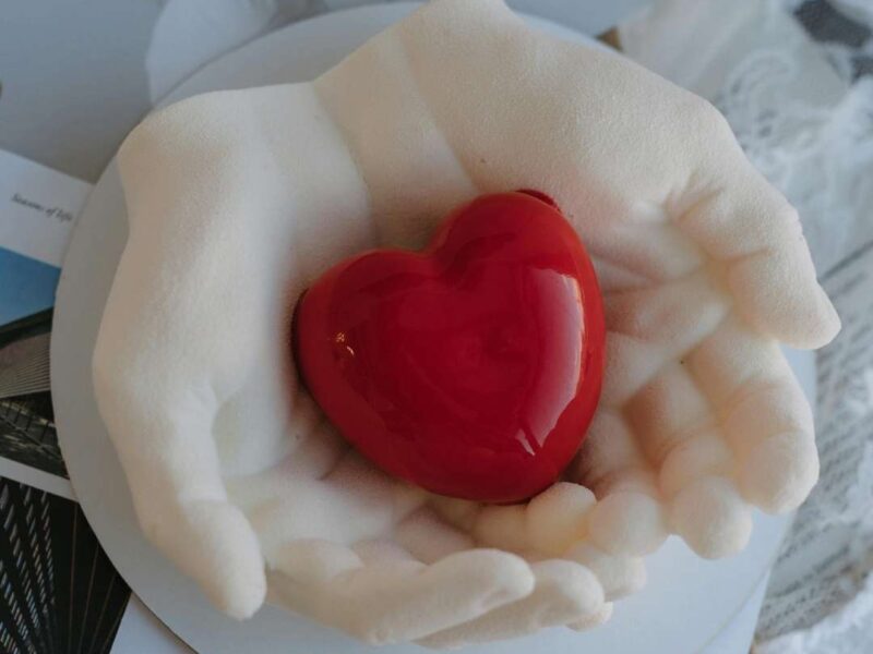 Aesthetic-Valentine’s-Day-wallpaper-featuring-a-stylish-woman-in-red-lying-gracefully-on-a-romantic-background- alongside-hands-forming-a-heart-shape-on-a-white-plate-conveying-love-and-Valentine’s-Day-mood.