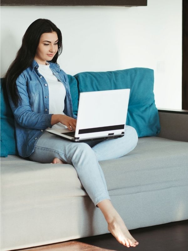 A-woman-sitting-on-the-couch-while-carrying-her-laptop-and-she-is-wearing-jeans-touser-and-blue-jacket-as-her-15-work-from-home-outfit-ideas-for-women