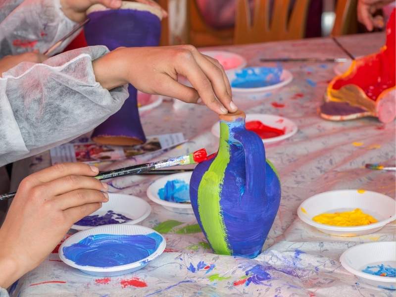 Featured-Image-Of-Clay-Ideas-showing-icture-of-a-young-child-painting-a-small-pottery-with-blue-and-green